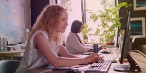 Women sitting at desk typing on laptop in office setting